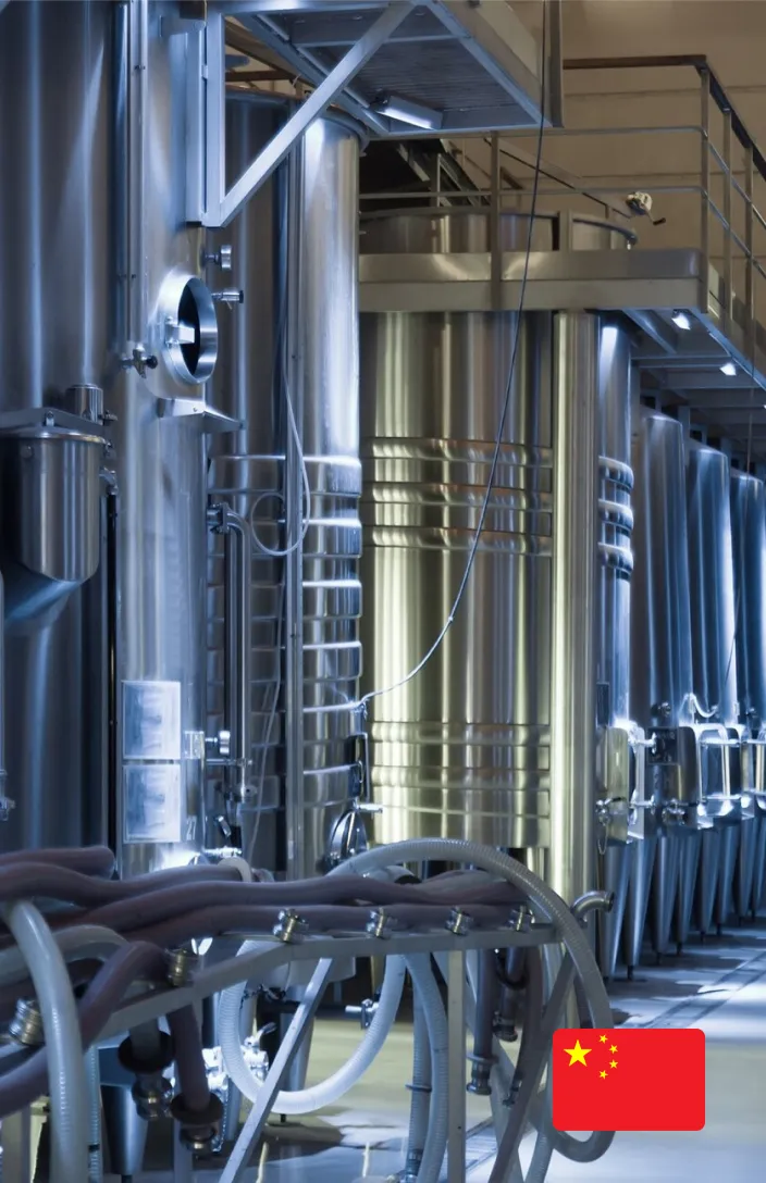 Interior of an industrial plant with multiple large, reflective tanks and complex piping systems